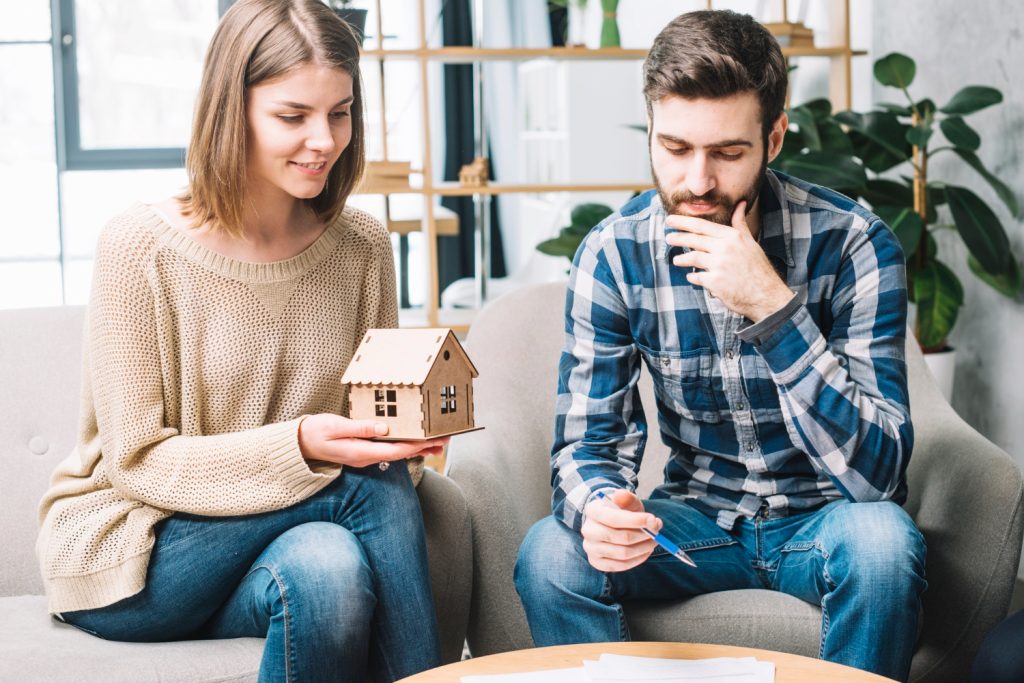 Couple discussing house model and paperwork in modern living room setting