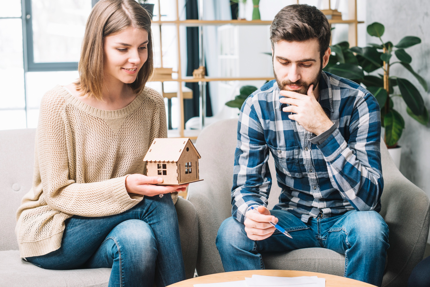 Couple discussing house model and paperwork in modern living room setting