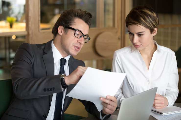 Business professionals discussing documents and using a laptop in a modern office setting